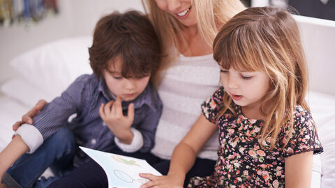 Frau sitzt mit 2 Kindern auf der Couch und liest vor