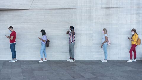 Gruppe von jungen Menschen warten auf den Gang in einen Ladenmarkt, während soziale Distanz in Linie während Coronavirus Zeit halten