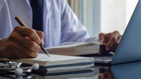 Arzt sitzt mit Büchern am Laptop und macht sich Notizen