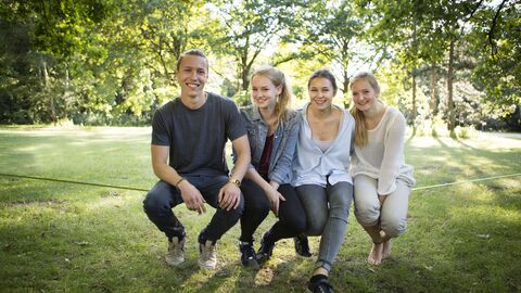 4 Jugendliche sitzen auf einer im Park gespannten Slackline 4 Jugendliche sitzen auf einer im Park gespannten Slackline
