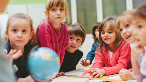 Kindergartenkinder sitzen vor einem Globus