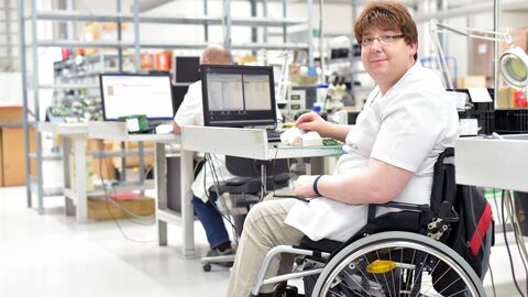 Behinderter Arbeitnehmer in einem Rollstuhl, Montage von elektronischen Komponenten in einer modernen Fabrik am Arbeitsplatz Behinderter Arbeitnehmer in einem Rollstuhl, Montage von elektronischen Komponenten in einer modernen Fabrik am Arbeitsplatz
