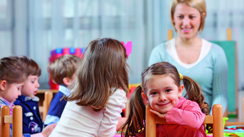 Kindergartenkinder sitzen mit einer Erzieherin am Tisch