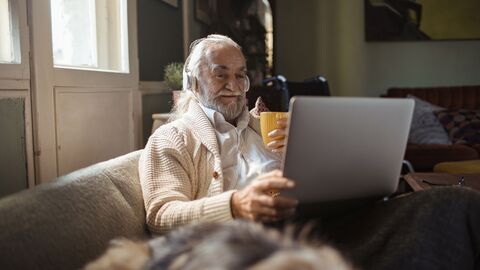 Senior mit Laptop sitzt auf einer Couch