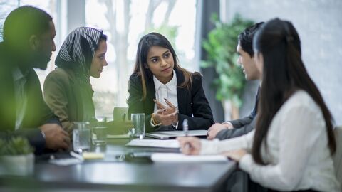 Fünf Personen unterschiedlicher Herkunft sitzen an einem Tisch und unterhalten sich