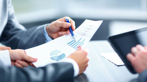 Hände von drei Personen in Business-Anzügen auf einem Tisch halten mit Diagrammen bedruckte Papiere