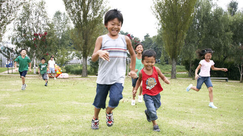 Kinder asiatischer Herkunft spielen auf einer Wiese Fußball
