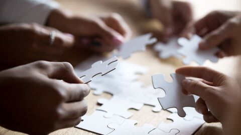 Nahaufnahme von Händen eines multirassischen Teams, die ein weißes Puzzle zusammensetzen