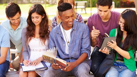 Highschool-Schüler arbeiten an einem Projekt auf dem Campus und sitzen nebeneinander und halten ein digitales Tablet und ein Lehrbuch