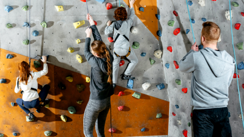 Gesichert von Jugendlichen üben Kinder an einer Kletterwand Gesichert von Jugendlichen üben Kinder an einer Kletterwand