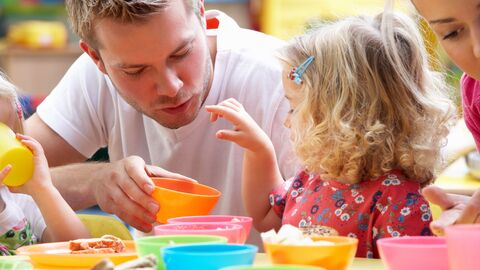 Erzieher im Kindergarten mit einem kleinen Mädchen an einem Tisch