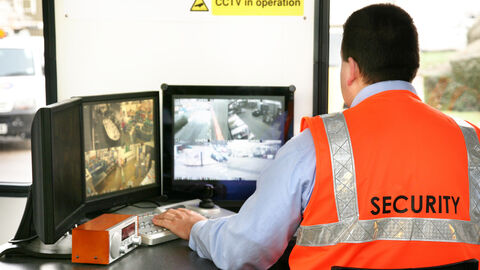 Arbeiter sitzt mit Schutzweste vor Überwachungsmonitoren