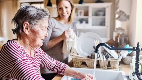 Seniorin spült Geschirr, eine junge Frau trocknet das Geschirr ab