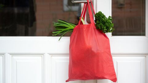 Eine mit Gemüse gefüllte rote Einkaufstausche hängt an einer geschlossenen Haustür