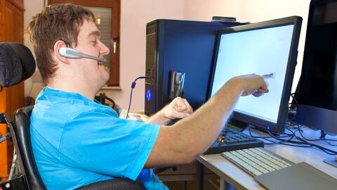 Ein schwerbehinderter Mann sitzt im Rollstuhl an einem Computer