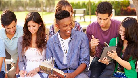Jugendliche sitzen im Park auf einer Mauer und unterhalten sich.