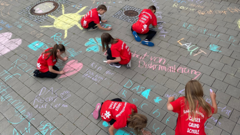 Schülerinnen und Schüler der Gönser Grundschule aus Butzbach malen Kreidebotschaften zum Thema Kinderrechte vor das Hessische Ministerium für Soziales und Integration