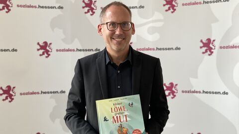 Minister Kai Klose hält das Kinderbuch "Kleiner Löwe, großer Mut" in den Händen.