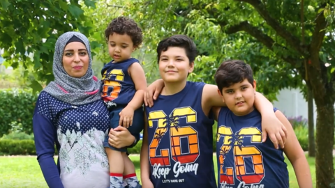 Familie mit Mutter und drei Kindern steht auf einer grünen Wiese vor Bäumen