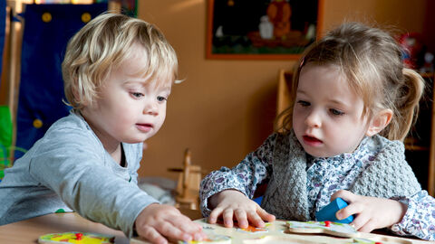 Zwei Kleinkinder sitzen am Tisch und spielen Zwei Kleinkinder sitzen am Tisch und spielen
