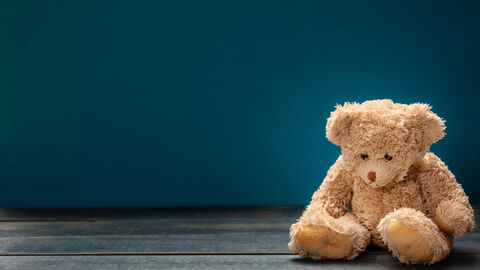 Ein Teddybär sitzt in einem leeren Zimmer auf dem Boden und schaut traurig nach unten