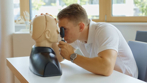 Ein Medizinstudent untersucht das rechte Auge einer Trainigspuppe