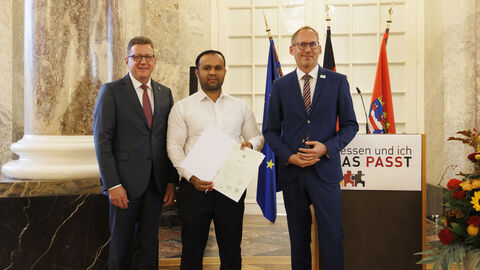 Einbürgerungsfeier 2023: Zeeshan Gull Minister Klose und Staatssekretär Sauer mit Zeeshan Gull bei der Einbürgerungsfeier. Gull hält die Einbürgerungsurkunde in den Händen.