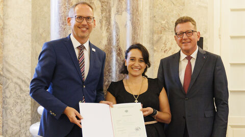 Einbürgerungsfeier 2023: Nikoleta Ioannidou Minister Klose und Staatssekretär Sauer mit Nikoleta Ioannidou bei der Einbürgerungsfeier. Ioannidou hält die Einbürgerungsurkunde in den Händen.