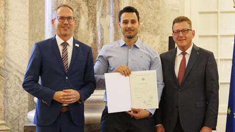 Einbürgerungsfeier 2023: Achref Kassebi Minister Klose und Staatssekretär Sauer mit Achref Kassebi bei der Einbürgerungsfeier. Kassebi hält die Einbürgerungsurkunde in den Händen.