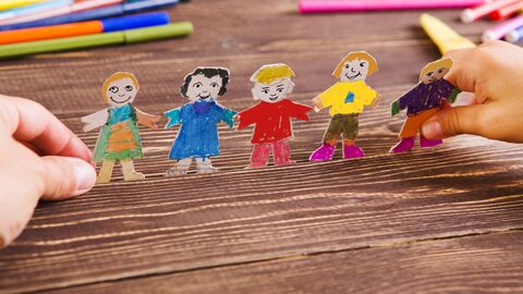 Zwei Kinderhände halten eine Girlande aus Papier mit ausgeschnittenen Menschen. Auf dem Tisch liegen bunte Filzstifte. Zwei Kinderhände halten eine Girlande aus Papier mit ausgeschnittenen Menschen. Auf dem Tisch liegen bunte Filzstifte.