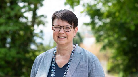 Portrait von Regine Bresler, sie steht im Freien vor Bäumen und lächelt.