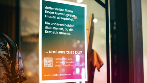 Schaufensterscheibe mit Plakat „GEWALT GEGEN FRAUEN“ Nahaufnahme einer Schaufensterscheibe, hinter der formatfüllend das Kampagnenmotiv „GEWALT GEGEN FRAUEN“ angebracht ist