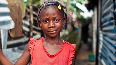 Afrikanisches Mädchen steht an einer Baracke, hält Dollarscheine in der Hand