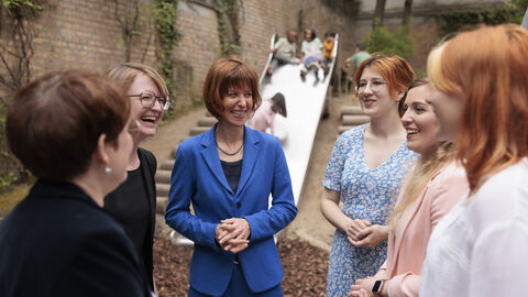 Sozialministerin Hofmann mit Erzieherinnen der Kindertagesstätte „Scharnhorststraße“ in Wiesbaden Sozialministerin Hofmann inmitten einer Gruppe Frauen. Im Hintergrund spielen Kinder auf einer Rutsche.
