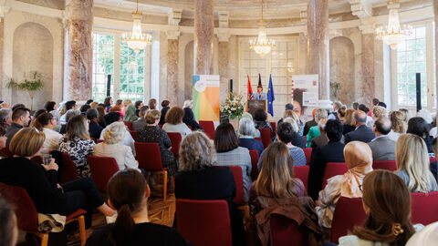Ein Saal indem eine Rede gehalten wird. Das Publikum ist von hinten zu sehen.