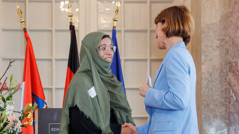 Ministerin Hofmann überreicht einer Frau eine Urkunde und schüttelt ihre Hand.
