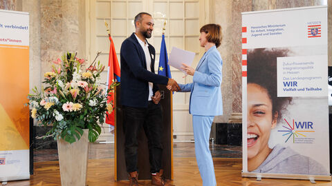 Ehrenamtlich aktive Integrationslotsinnen und -lotsen Ministerin Hofmann überreicht einem Mann eine Urkunde und schüttelt seine Hand.