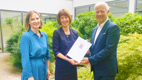Die Landesbeauftragte zur Förderung und Beteiligung von Kindern und Jugendlichen, Miriam Zeleke, Sozialministerin Heike Hofmann und Thomas Domnick,  Erster Vorsitzender des Vereins Ombudsstelle für Kinder- und Jugendrechte in Hessen e.V. (v.l.)  Miriam Zeleke, Sozialministerin Heike Hofmann und Thomas Domnick stehen nebeneinander und halten den Bescheid zur Förderung in der Hand.
