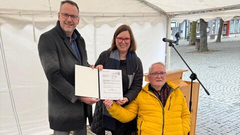 Bürgermeister Markus Boucsein, Sozialstaatssekretärin Manuela Strube sowie Initiator Robert Weck halten gemeinsam den Bescheid in den Händen