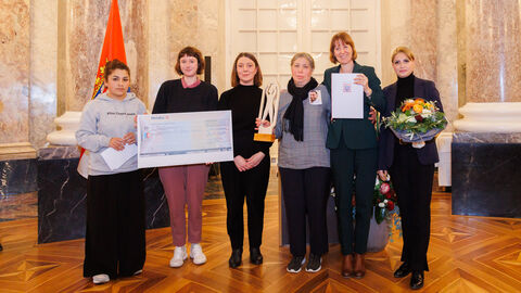 Integrationspreis 2024 Mehrere Frauen stehen nebeneinander. Manche von Ihnen halten ein Schild, dass eine Überweisung zeigt. Eine andere Frau hält einen Pokal.