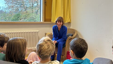 Sozialministerin Heike Hofmann liest Kindern in der Kita Am Zahlwald in Roßdorf vor Sozialministerin Heike Hofmann sitzt fröhlich lächelnd auf einem Stuhl. Vor ihr im Publikum sieht man vier auf sie gerichtete Kinderköpfe.
