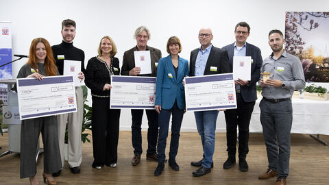 Preisverleihung Gruppenfoto Integration Mehrere Menschen blicken in die Kamera, einige halten sehr große Schecks.