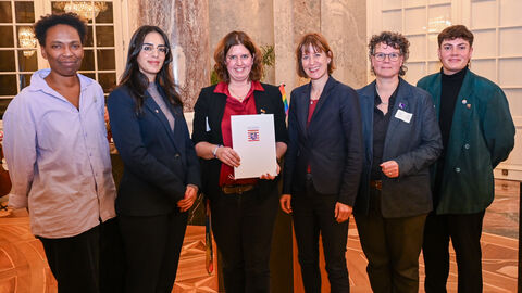 Mehrere Frauen stehen zusammen und lächeln in die Kamera. Eine hält eine Mappe mit dem Hessen-Wappen darauf