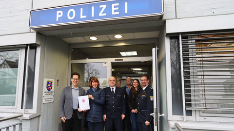 Mehre Personen stehen in Türeingang. Überhalb der Tür befindet sich ein blaues Schild auf dem "Polizei" steht. 