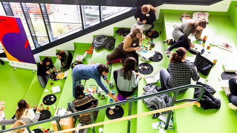 Kulturkita Blick auf eine grüne Treppe auf der viele Personen verteilt sitzen und malen und basteln.