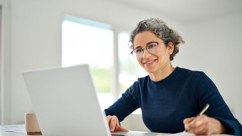 Frau schaut in Laptop und macht Notizen