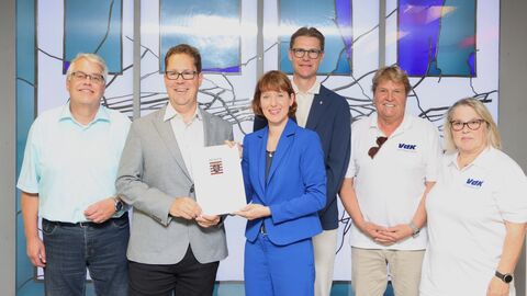 Sechs Personen stehen nebeneinander und zwei Personen halten ein Din A4 Dokument hoch.