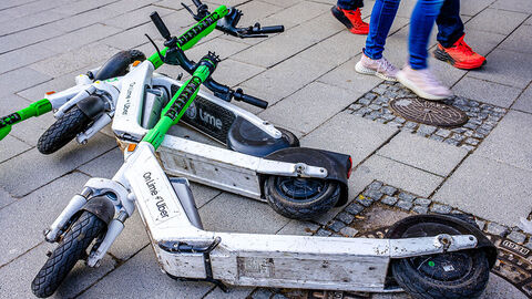 E-Roller liegen auf dem Gehweg Mehrere E-Roller liegen auf einem Gehweg. Passanten laufen an ihnen vorbei.