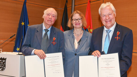 Staatssekretärin Hechler händigt Bundesverdienstorden an Gerd Thomas aus Usingen und Prof. Christian-Dietrich Schönwiese aus Oberursel aus Zwei festlich gekleidete ältere Herren haben ein Verdienstorden an ihrem Jacket und halten Urkunden in die Kamera. In ihrer Mitte steht eine Frau.