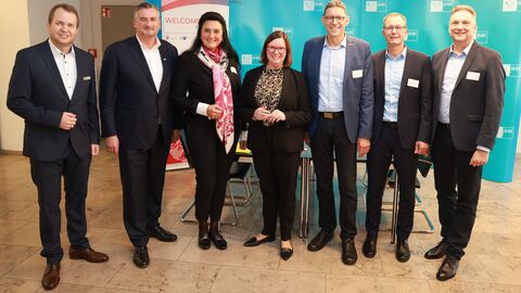 Staatssekträtin Strube steht gemeinsam mit einer Gruppe Personen vor einem Infostand der IHK.